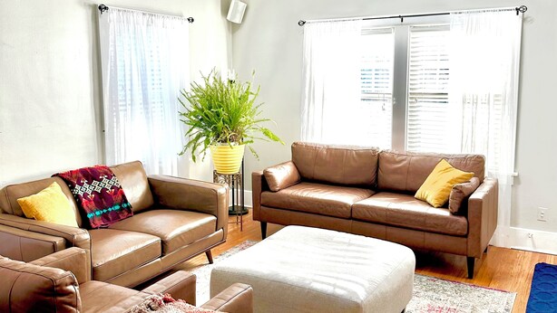 A spacious living room with a high ceiling, two brown leather sofas, a coffee table, and a ceiling fan.