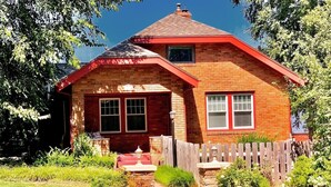 A two-story brick house with a red roof, a front porch, and a wooden fence.