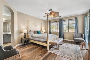 Quarto com cama de dossel, ventilador de teto, cadeira, escrivaninha e janela com cortinas.