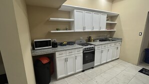 Una cocina compacta con gabinetes blancos, una estufa a gas, un microondas y un cubo de basura.