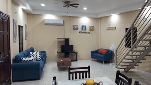 Una sala de estar con un sofá azul, una mesita, un televisor y una escalera.