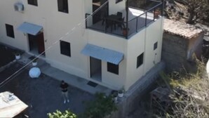 Un edificio de dos pisos con un balcón en el nivel superior, techo plano y un pequeño patio.