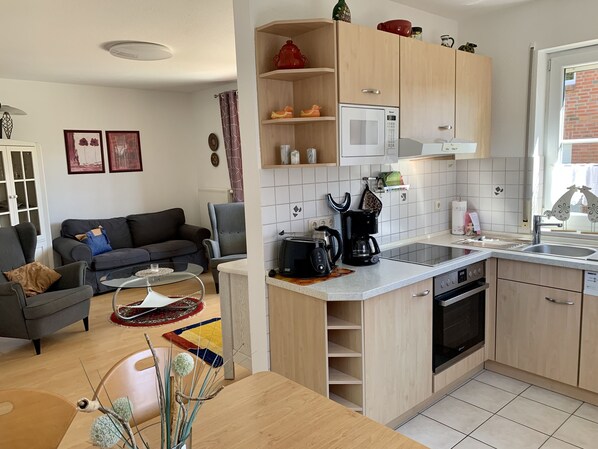 A compact kitchen with a microwave, coffee maker, and oven. A dining table with a vase of dried plants is in the foreground.