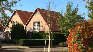 Ein Wohnhaus mit rotem Ziegeldach, einem sichtbaren Fenster und einem gepflegten Garten mit verschiedenen Pflanzen und Blumen.