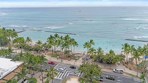 Blick auf einen Strand mit Palmen, einer Straße und dem Meer.