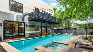 A modern outdoor pool area with a built-in hot tub, lounge chairs, and a covered seating area.