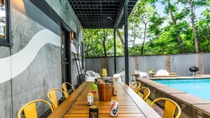 An outdoor dining area with a wooden table, yellow chairs, and a pool in the background.