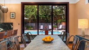 A dining area with a marble table, chairs, a bowl of fruit, and a view of a swimming pool.
