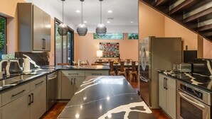 A modern kitchen with a central island, stainless steel appliances, pendant lighting, and a dining area with a colorful backsplash.