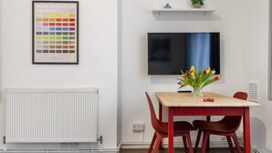 Ein moderner Essbereich mit einem Holztisch, roten Stühlen, einer gerahmten Farbpalette, einem Flachbildfernseher und einer kleinen Pflanze auf einem Regal.