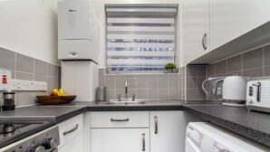 Eine moderne Küche mit weißen Schränken, einem Backofen, einem Kochfeld, einer Spüle und einem Fenster mit Jalousien.