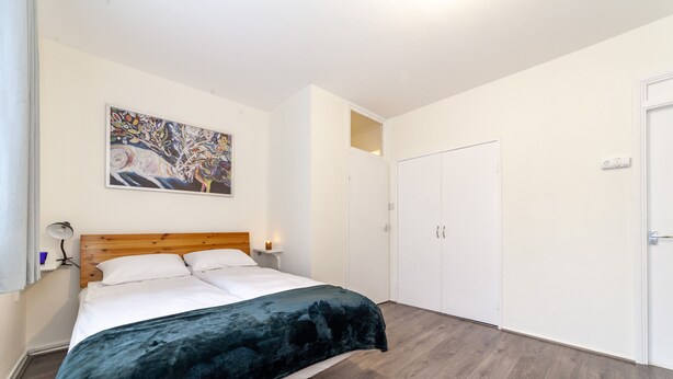 Ein Schlafzimmer mit einem Bett, einem Holz-Kopfteil, einem Bild an der Wand, einem Kleiderschrank und einer Tür.