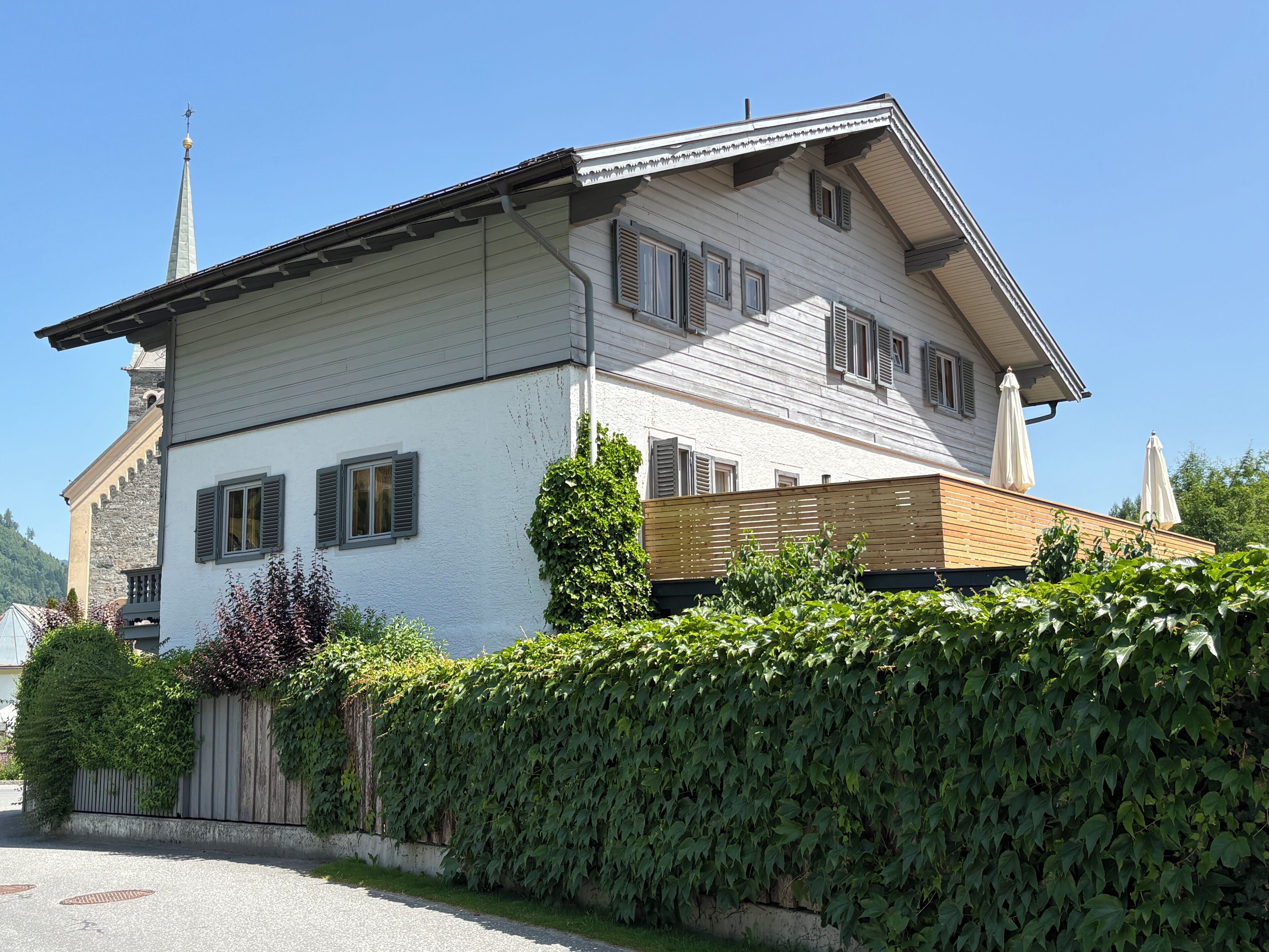 Une maison à deux étages, dotée d’un toit à forte pente, d’une cheminée bien visible et d’une petite structure en forme de tour sur le toit.