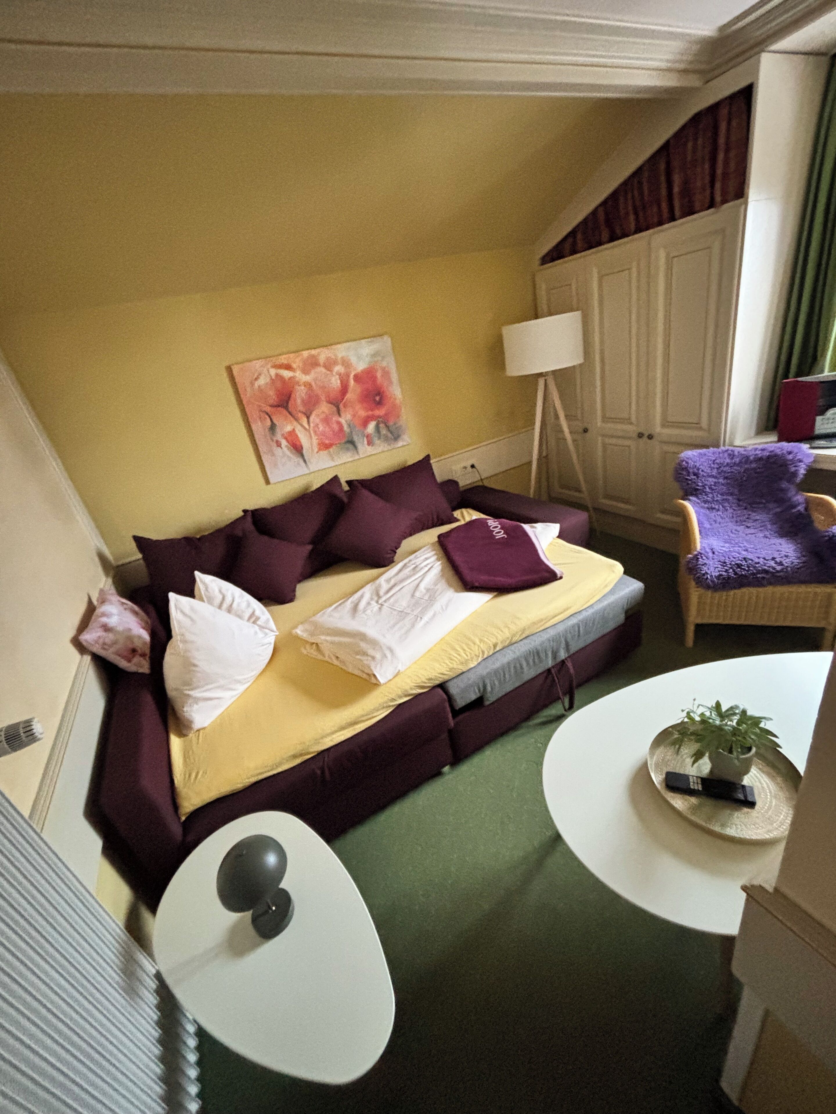 Et hotelværelse med en seng, et lille bord, en stol, en lampe og et billede på væggen.