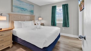 Ein Hotelzimmer mit Bett, Nachttisch, Lampe, einem Gemälde, einem Fenster mit Vorhängen und einer Tür.