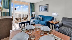 Ein Zimmer mit Esstisch für vier Personen, einem blauen Sofa, einem gemusterten Sessel und einem Balkon mit Blick.