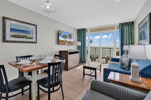 A dining area with a table set for four, a sofa, a small table, and a balcony with a view.