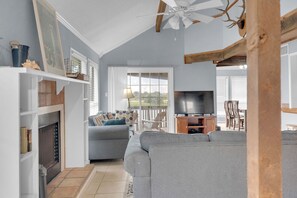 Un salon avec une cheminée, un canapé, un téléviseur et un ventilateur de plafond.