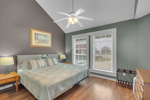 A bedroom with a bed, nightstands, a ceiling fan, a window with blinds, and a wooden dresser.