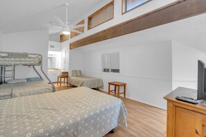Ein Zimmer mit Etagenbetten, einem Schreibtisch, einem Sessel, einem Fernseher und einem Deckenventilator.