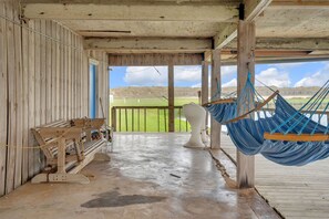 Ein Zimmer aus Holz mit einer Bank, einer Hängematte und Blick auf ein Wiesenfeld.