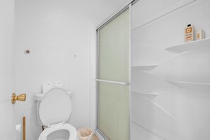 A bathroom with a toilet, a shower enclosure, and a shelf with toiletries.