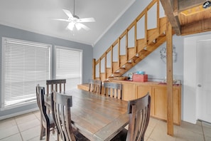 Un coin repas avec une table et des chaises en bois, un ventilateur de plafond et un escalier en bois.