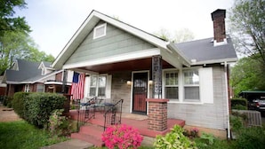 A two-story house with a front porch, a brick chimney, and a small garden with pink flowers. - The Jackson (Nashville)