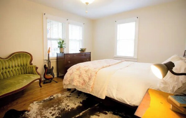 Une chambre à coucher avec un lit, un fauteuil vert, une guitare, une commode et une lampe.