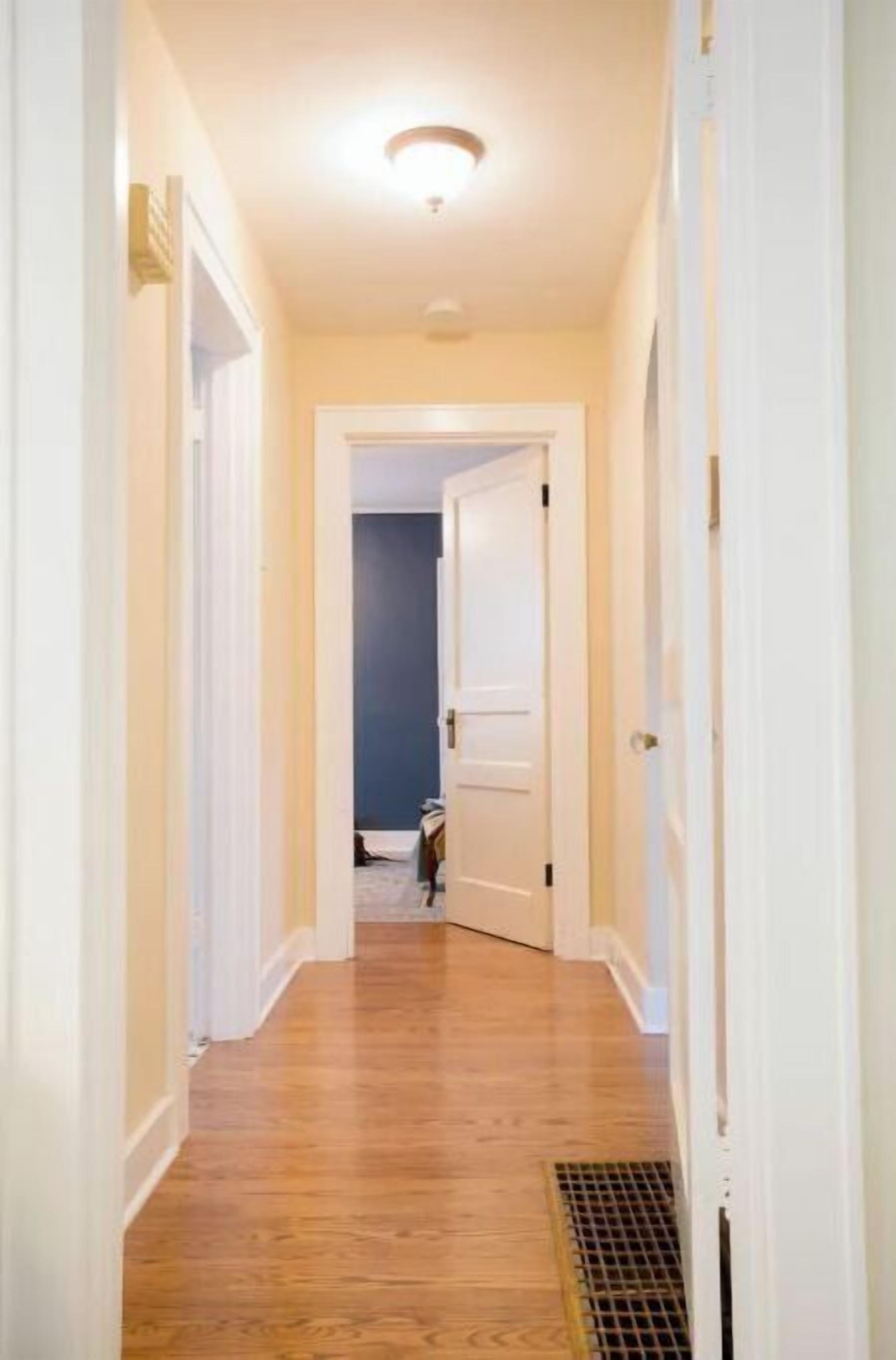 A narrow hallway with wooden flooring and white walls.