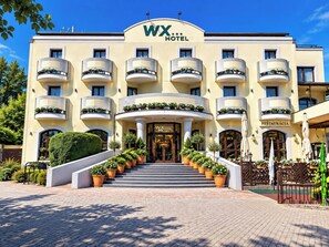 A hotel with a central entrance, multiple balconies with plants, and a sign indicating a restaurant. - WX Hotel (Bratislava)
