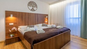 A hotel room with a wooden headboard, a bed with white linens, a brown bedspread, and a wall-mounted tree decoration. - WX Hotel (Bratislava)