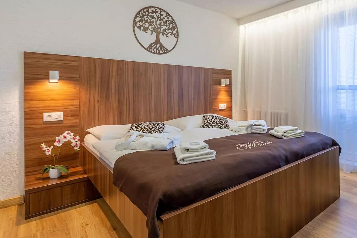 A hotel room with a wooden headboard, a bed with white linens, a brown bedspread, and a wall-mounted tree decoration.