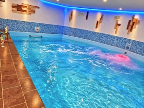Una piscina interior con mosaicos azules, un detalle de pared de madera y suelo de baldosas.