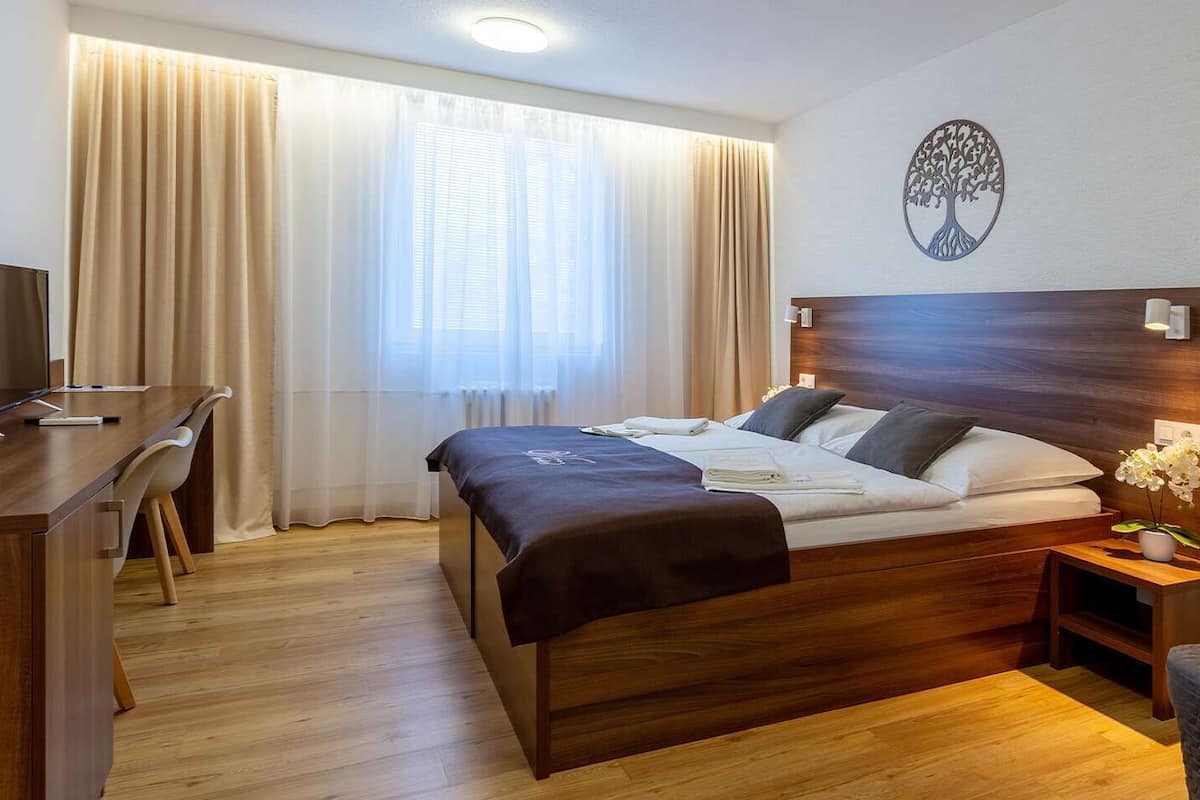 A neatly arranged hotel room with a bed, bedside table, TV, desk, and chair.