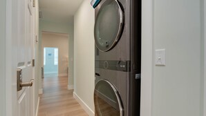 Uma lavanderia com duas máquinas de lavar e secar de abertura frontal, piso de madeira e uma porta com fechadura.