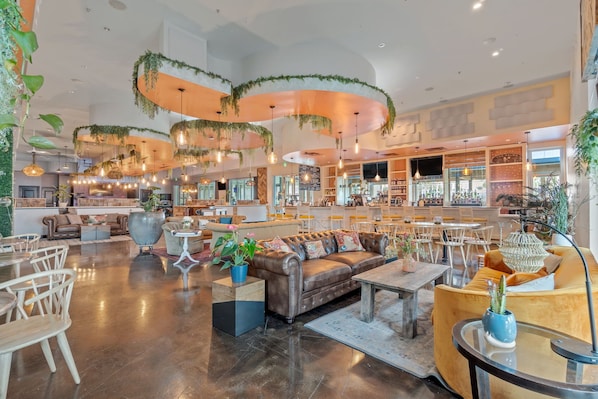 A spacious lobby with a leather sofa, wooden chairs, and a bar area.