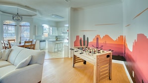 Een moderne woonkamer met een tafelvoetbalspel, een witte bank en een keuken op de achtergrond.