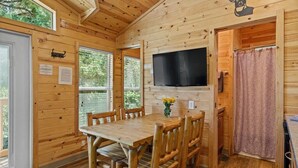 Ein Holzblock-Interieur mit Esstisch, Stühlen, einem Flachbildfernseher und einer Duschgelegenheit.