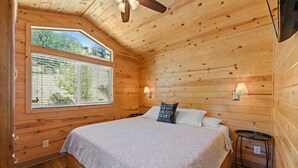 Ein Schlafzimmer einer Holzhütte mit Bett, Fenster, Deckenventilator und Nachttisch.