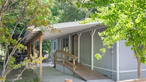 A covered outdoor area with a wooden ramp leading to a building, surrounded by trees and a fence.