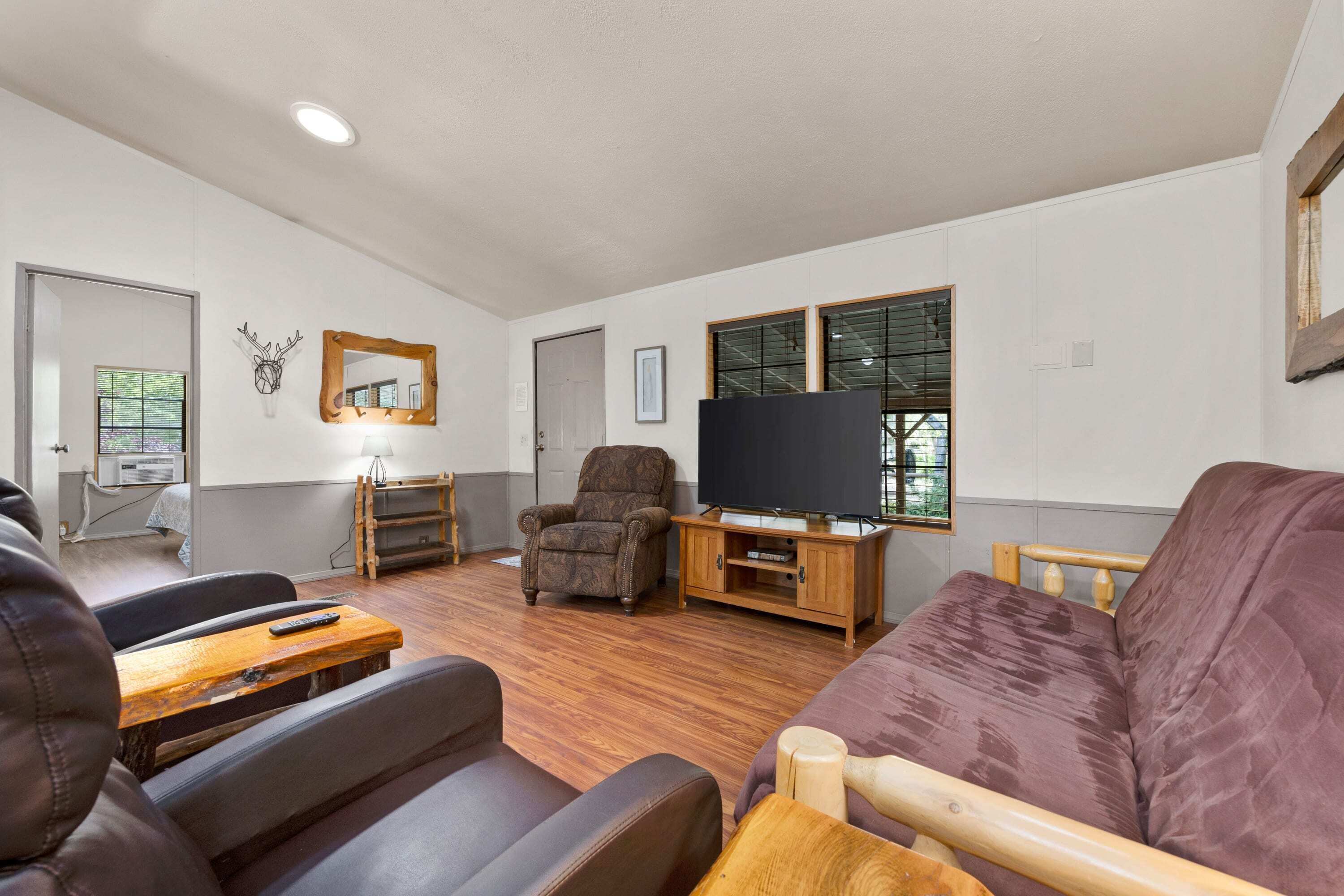 A living room with a sofa, a chair, a TV stand, and a wooden table.