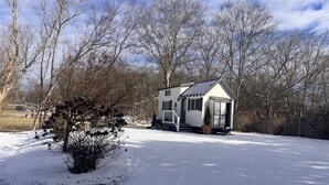 Ein kleines, eingeschossiges Haus mit Satteldach, umgeben von verschneiteter Erde und kahl stehenden Bäumen.