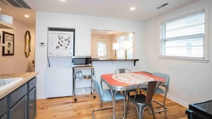 Cocina compacta con microondas, tostadora y lavamanos. Zona de comedor con mesa y sillas.