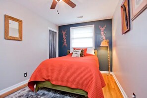 Une chambre à coucher avec un lit, un ventilateur de plafond, une fenêtre et une lampe sur pied.