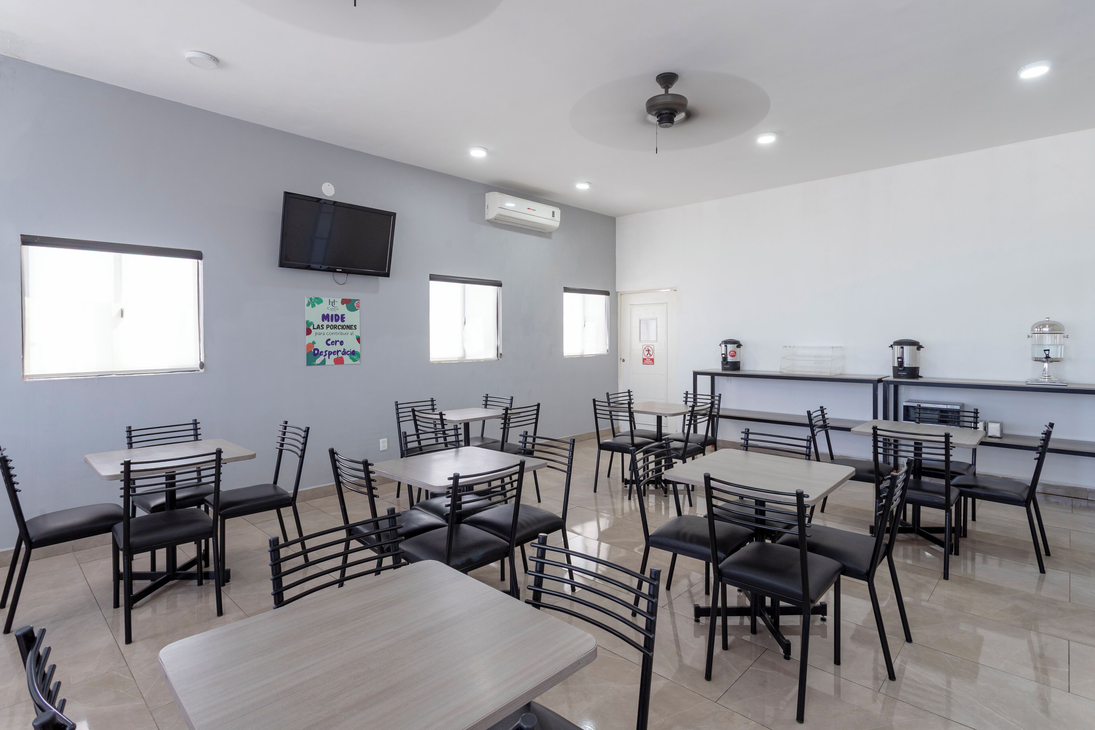 A dining area with multiple tables and chairs, a television mounted on the wall, and an air conditioning unit.