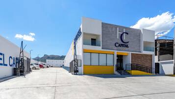Un hotel moderno con un llamativo letrero que dice 'Capital Hotel', una zona de estacionamiento y montañas al fondo.