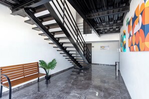 A modern interior with a wooden bench, a staircase, and a colorful wall mural. - Capital Hotel Saltillo (Saltillo)