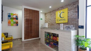 Un hall d’hôtel avec un mur en briques, une enseigne « Hotel Capital Hotel », un comptoir d’accueil, une plante et une œuvre d’art abstraite aux couleurs vives.
