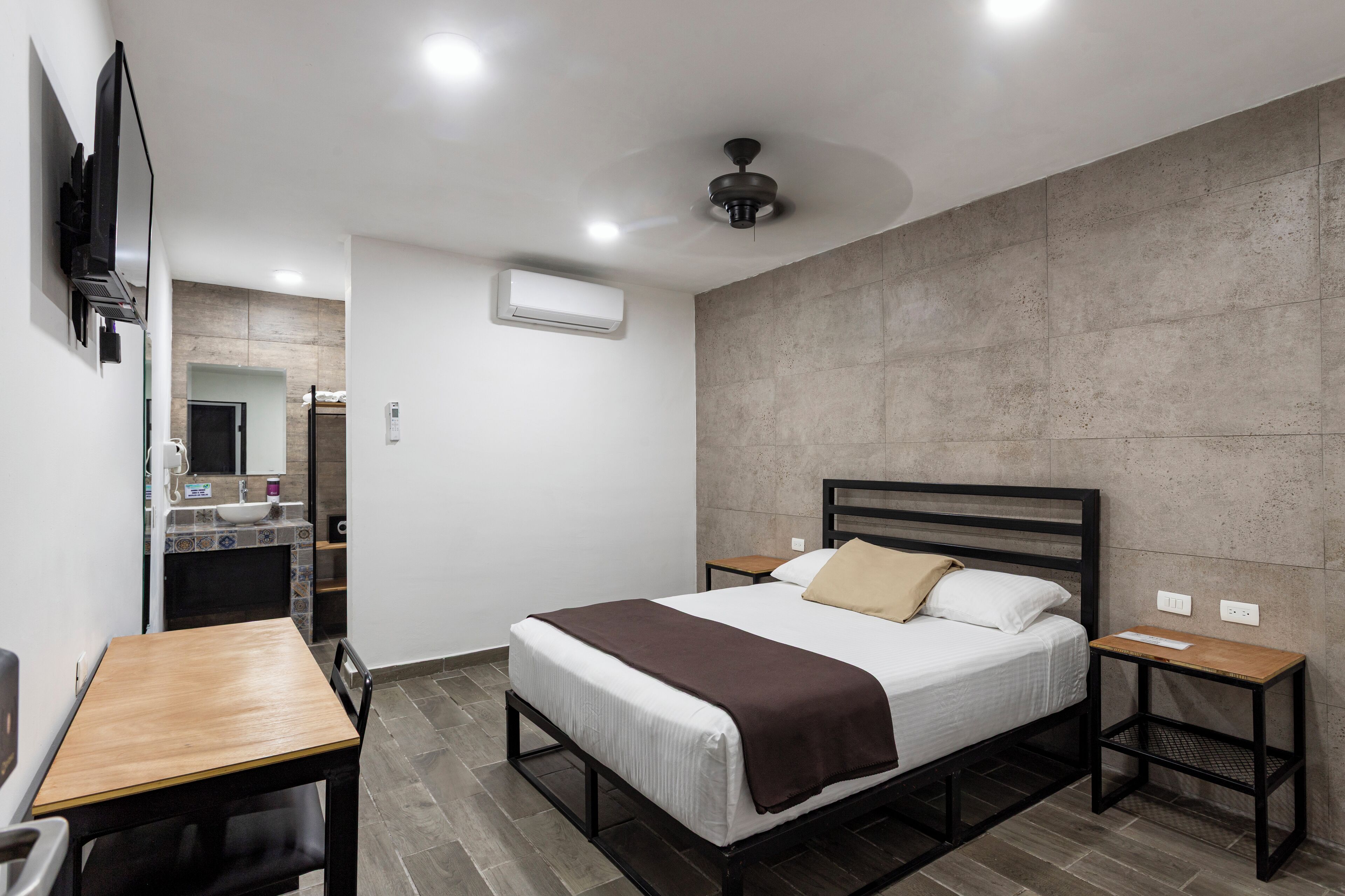 Un dormitorio moderno con cama, mesitas de noche, un escritorio y una televisión.